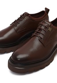 Bruine leren veterschoenen met dikke, geribbelde rubberen zolen en een klein lusje aan de achterkant.