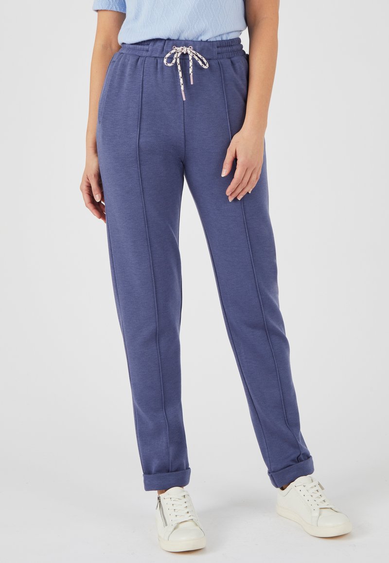 Blaue Sweatpants aus weichem Material mit einem Kordelzugbund, ausgestattet mit Seitennähten und umgeschlagenen Bündchen, kombiniert mit weißen Sneakers.