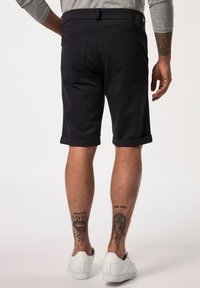 Tmavě modré šortky s ohrnutými manžetami, vyrobené z hladkého materiálu, se dvěma zadními kapsami. Čistý design a nošeny s bílými teniskami.