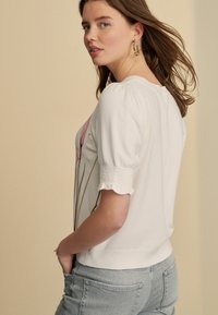 Witte korte mouwen trui met bloemenpatroon, gestructureerde pofmouwen en ribbelomslag, gecombineerd met lichtblauwe denim. Eenvoudig en casual.