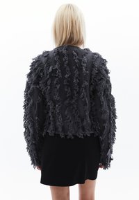 Svart kortärmad cropped tröja med texturerad, fransad detalj som löper vertikalt över ryggen. Mjukt, stickat material.
