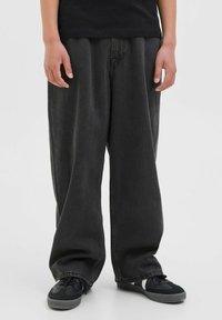 Pantalons en denim noir à jambe large avec une texture décolorée, présentant un design classique à cinq poches et des détails de couture discrets. Assortis à des baskets noires.