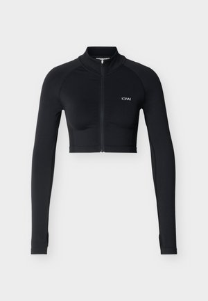 Μαύρο αθλητικό μπουφάν cropped με μακριά μανίκια, εμπρόσθιο φερμουάρ και μικρό λευκό λογότυπο στο αριστερό στήθος, εμφανιζόμενο σε απλό φωτεινό φόντο.