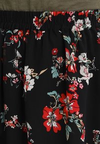 Jupe noire à motifs floraux avec une taille froncée, présentant des fleurs rouges, roses et blanches sur fond sombre. Tissu au toucher lisse.