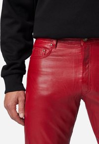 Rode leren broeken met een gladde textuur, met een slim fit, voorzakken en metalen studs. Gecombineerd met een zwarte sweatshirt.