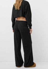 Czarny, prążkowany, skrócony sweatshirt w połączeniu z szerokimi czarnymi spodniami; miękka tekstura, luźny krój i dyskretny detal w pasie.