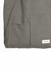 Pregača s okomitim prugastim uzorkom u tamnosivoj, bež i bijeloj boji, s dva prednja džepa i naljepnicom na kojoj piše "The Organic Company".