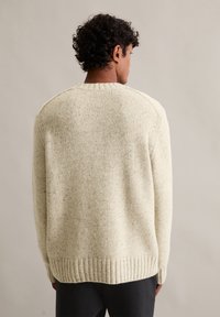 Suéter de malha de cor creme com um tecido texturizado, bainha canelada e ombros caídos. Apresenta um colarinho redondo clássico e um ajuste solto.