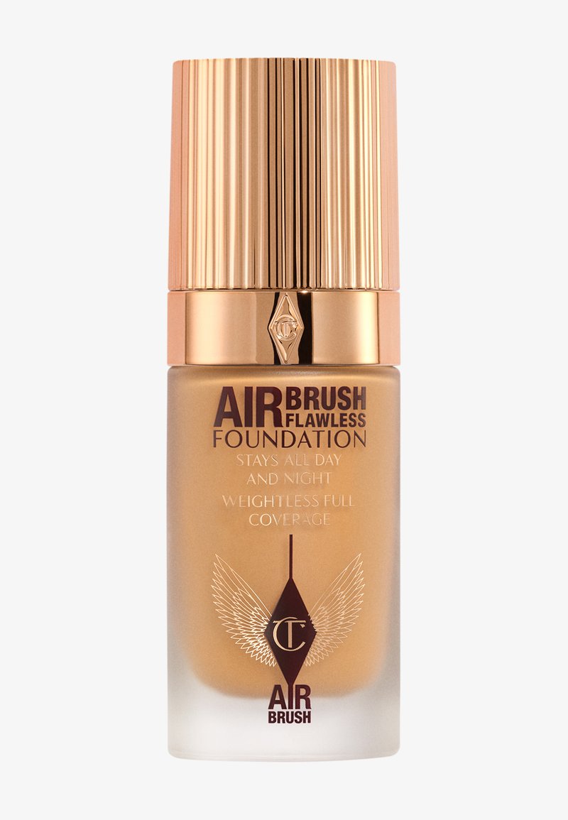 Gold and clear glass foundation bottle, ribbed gold cap, brown label with white text, features a logo and details on coverage and longevity.