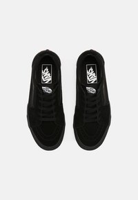 Black sneakers with a suede upper, featuring black laces, white logo on the tongue, and white stitching details along the sole.
