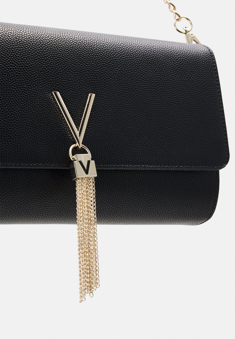 Pochette en cuir noir texturé avec une garniture en daim doré et un matériel unique en forme de V. Forme rectangulaire compacte avec fermeture à rabat.