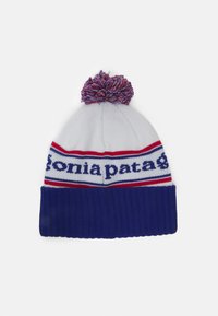 Strikket lue i hvit, blå og rød. Har en blå ribbestrikket mansjett og en flerfarget dusk på toppen. "patagonia"-logoen er synlig.