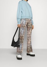 Felpa blu chiaro con una vestibilità comoda, pantaloni a campana con stampa serpente in toni terra e scarpe platform bianche chunky. Borsa nera.
