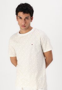 Šortspēļu ar īsām piedurknēm, apaļo kakla izgriezumu, gaismas bēšā krāsā ar ģeometrisku rakstu. Uz kreisā krūts ir neliels daudzkrāsains logo.