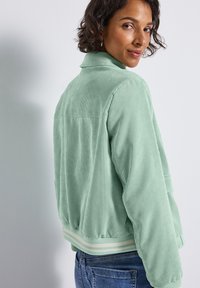 Hellgrüne Cordjacke mit Kragen, geripptem Saum mit zwei weißen Streifen und lässigem Schnitt. Nahtdetails verleihen Textur.