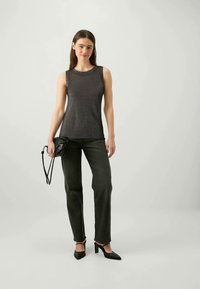 Black sleeveless top with a smooth texture, paired with dark green straight-leg jeans and black pointed-toe heels, holding a small black bag.