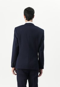 Námořnická obleková sako s dobře strukturovaným střihem, sezipními zadními ventily a knoflíkovými manžetami. Hladká tkanina, minimalistický design a čisté linie.