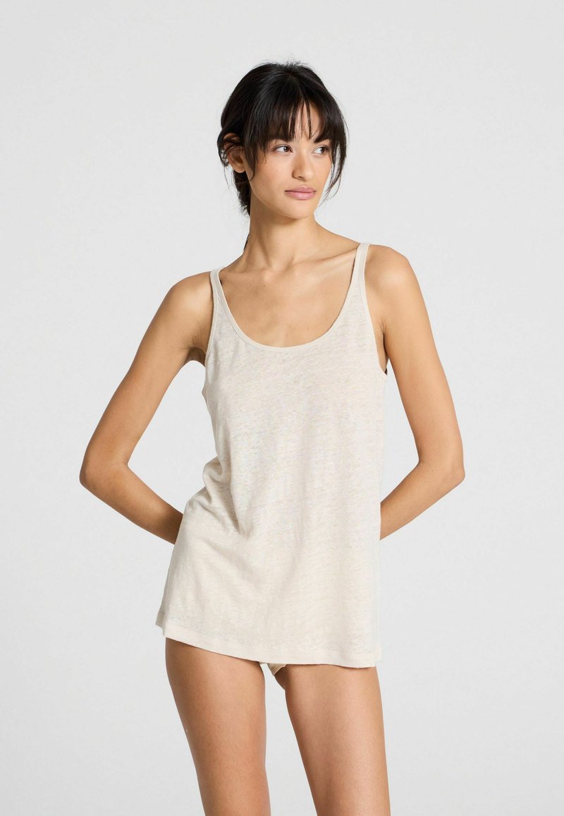 Top in un beige chiaro con vestibilità ampia, realizzato in un tessuto morbido e traspirante. Presenta spalline larghe e un scollatura arrotondata.