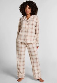 Flanellen pyjama set in beige met een lichtbruin ruitpatroon. Voorzien van lange mouwen, een bovenstuk met knopen en loszittende broek. Zachte textuur.