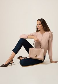 Beżowa skórzana torebka o zdefiniowanym kształcie, z detalami w kolorze złotym, połączona z jasnoróżowym swetrem i ciemnoniebieskimi klasycznymi dżinsami.