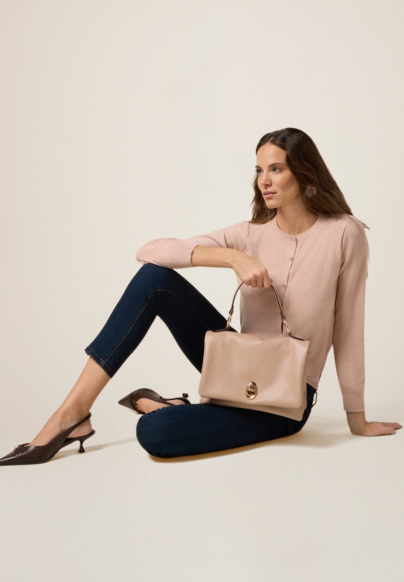 Beżowa skórzana torebka o zdefiniowanym kształcie, z detalami w kolorze złotym, połączona z jasnoróżowym swetrem i ciemnoniebieskimi klasycznymi dżinsami.