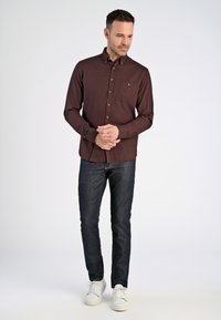 Camisa de manga larga color granate con botones y bolsillo, combinada con vaqueros oscuros y zapatillas blancas. Tejido suave con un ajuste estructurado.
