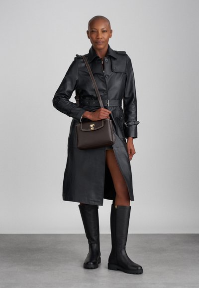 Black leather trench coat with buttons and a belted waist; paired with knee-high black boots and a small brown handbag with gold hardware.