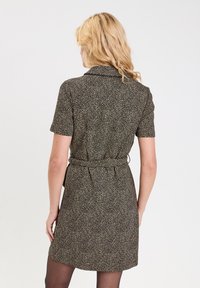 Robe à manches courtes en tissu noir avec un motif floral beige, dotée d'un col et d'une ceinture à la taille, longueur mi-cuisse.