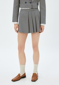 Falda corta de cuadros con pliegues en azul y blanco. Combinada con mocasines marrones y calcetines de canalé crema. Presenta una cintura ajustada.