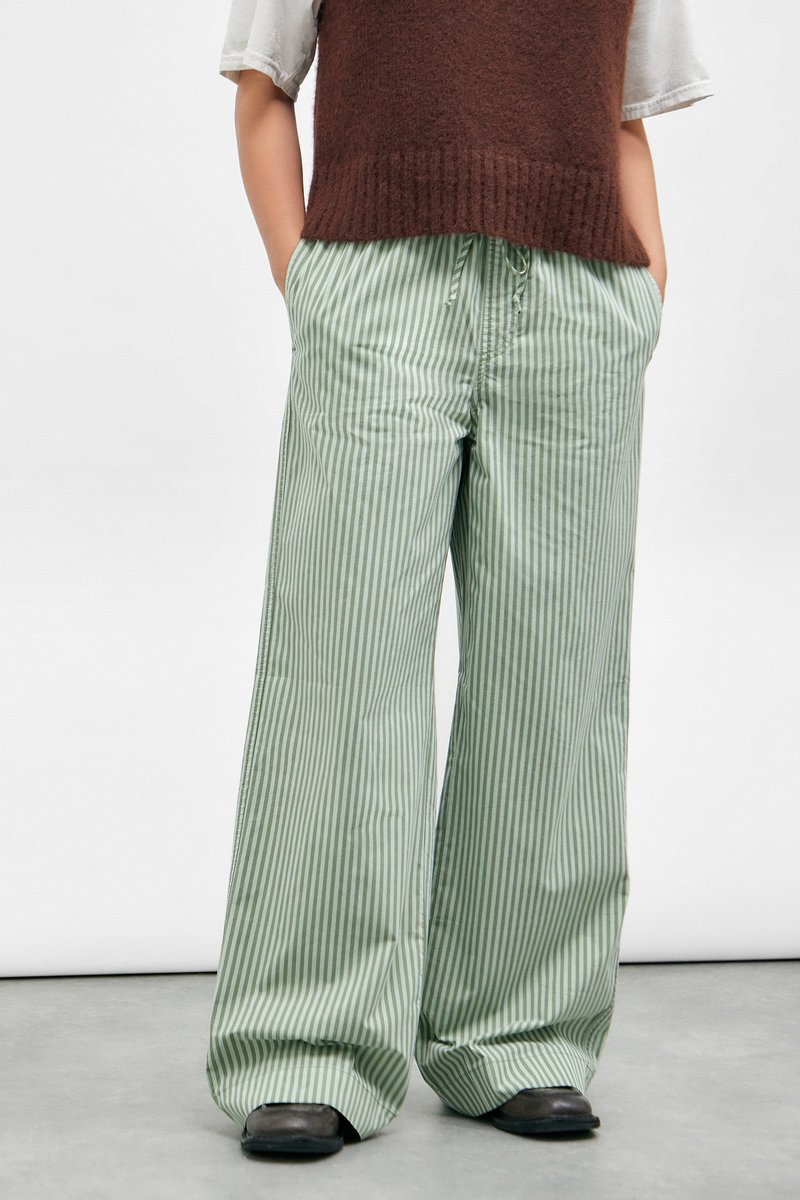 Striped wide-leg pants in light green and white fabric, featuring an elastic waistband and relaxed fit, paired with a brown knit top.