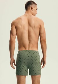 Zielone szorty wykonane z miękkiego materiału, z powtarzającym się małym wzorem. Widoczny pas i dopasowany krój widoczny z tyłu.