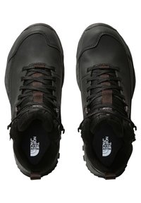 Zapatos de senderismo de cuero negro con una parte superior texturizada, cordones negros y suelas de goma, con un logo en la plantilla y una pestaña en el talón.