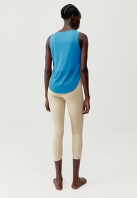 Blå atletisk tanktopp med rundet kant og beige leggings. Stoffet ser glatt ut med en tettsittende design og ingen synlige mønstre.