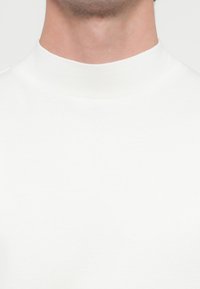 Biała bluza z kapturem typu mock neck wykonana z miękkiej tkaniny, charakteryzująca się bezszwową konstrukcją i gładką fakturą, zapewniającą czysty, minimalistyczny wygląd.