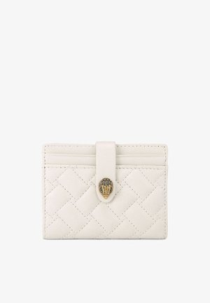 Porte-cartes en cuir blanc matelassé avec une bride et une fermeture décorative en laiton sur un fond uni.