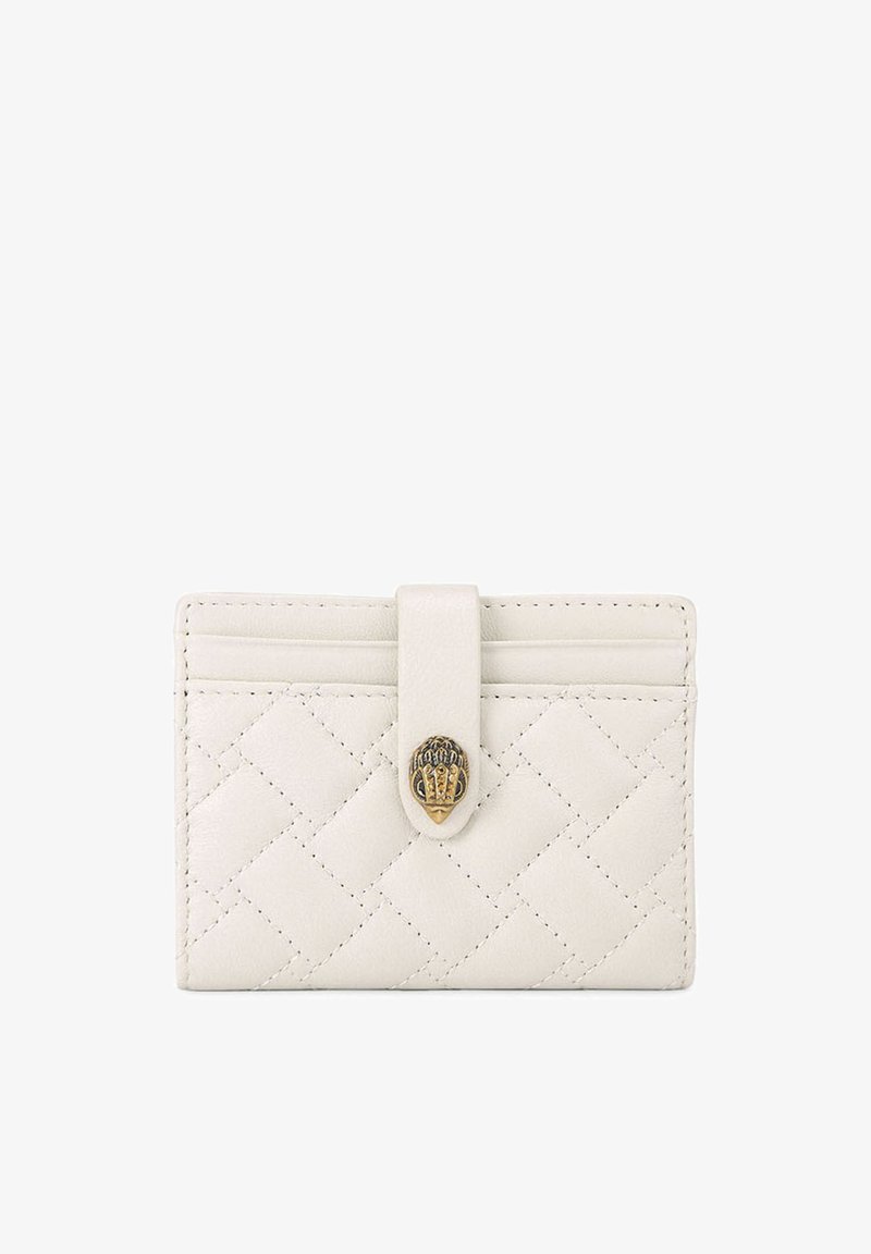 Porte-cartes en cuir blanc matelassé avec une bride et une fermeture décorative en laiton sur un fond uni.