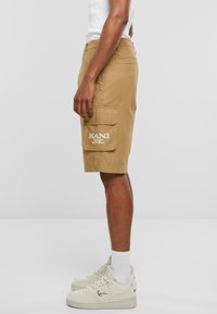 Khaki cargo šortky s bočnými vreckami, detailom loga a uvoľneným strihom. Skombinované s bielymi teniskami a členkovými ponožkami.