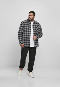 Rutete flanellskjorte i marineblått og hvitt, med knapp-down-design, kombinert med svarte cargo-bukser. Hvit t-skjorte under og hvite sneakers.