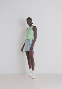 Mintgrön ärmlös topp, ljusblå jeanstub, vita sneakers med accenter. Släta texturer och figursydd design framhäver en avslappnad stil.
