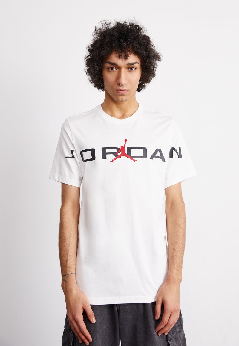 Tricou alb din bumbac cu mâneci scurte, având un grafic mare „JORDAN” de culoare neagră și un logo Jumpman roșu imprimate pe față.