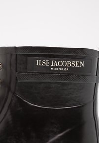 Černá gumová bota s texturovaným povrchem, vybavená značkovou etiketou "ILSE JACOBSEN NORNBAER" a metalovými očky pro šňůrky.