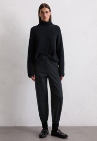 Knitted dark sweater with a high turtleneck and wide sleeves, paired with dark, tapered pants and black loafers. Textured fabric.