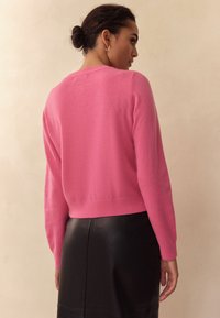 Fuchsia pink strikket trøje med rund hals og afslappet pasform, kombineret med en sort lædernederdel, der fremhæver glatte teksturer.