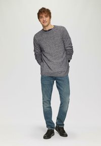 Grau gesprenkeltes Langarmshirt, blaue Jeans und schwarze Sneakers. Das Shirt hat einen runden Ausschnitt und leicht herunterhängende Ärmel.
