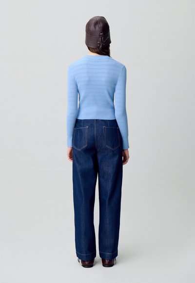 Pullover a coste di colore azzurro chiaro, con collo alto, abbinato a jeans a gamba larga blu scuro e un berretto di pelle marrone. Tessuto liscio e design semplice.