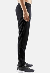 Sorte træningsbukser lavet af letvægtsstof, med taperet pasform, elastisk talje og sidelommer. Sammen med sorte sneakers.