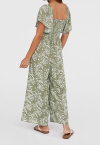 Mono verde con estampado floral, mangas cortas abullonadas, espalda cuadrada y cintura elástica. Tejido suave, piernas anchas, combinado con sandalias.