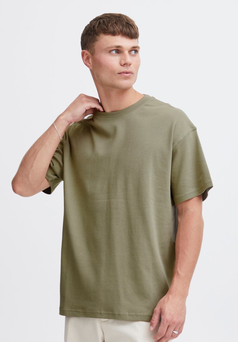 Tricou din bumbac verde măsliniu cu croială lejeră, guler rotund și mâneci scurte. Textură netedă, fără modele sau accente vizibile.