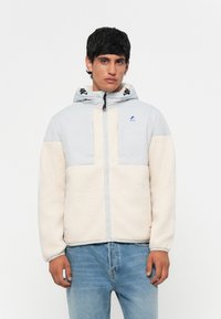 Light gray and cream zip-up jacket with a hood, featuring a fleece texture, front pockets, and a logo accent near the neckline.