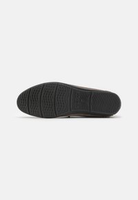 Zapato de ante marrón con una suela de goma negra con patrón, que presenta agujeros de drenaje y un agarre texturizado para mayor tracción.